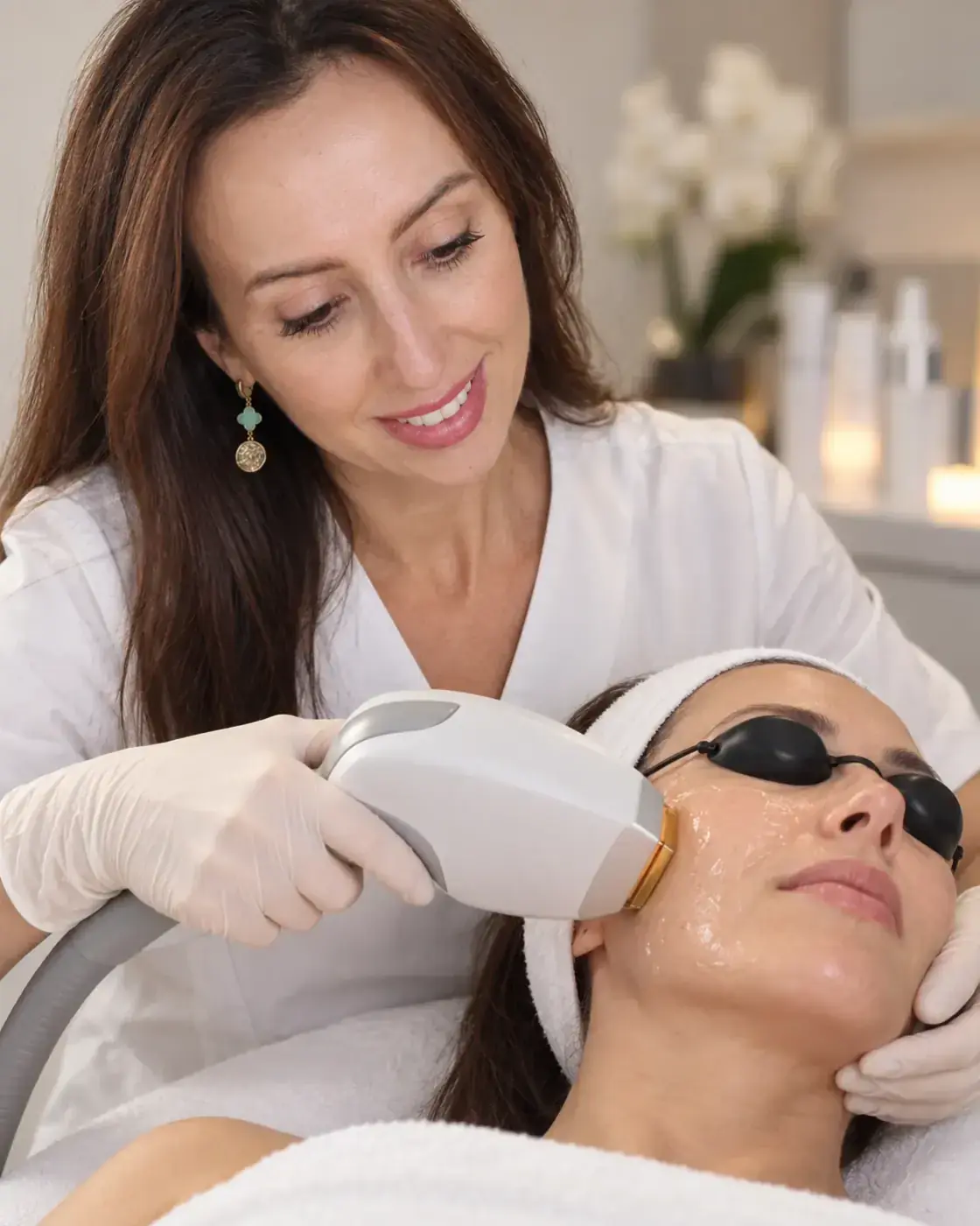 An IPL photofacial at Perfecta by Marina Stejar, North Scottsdale — the esthetician passing the IPL handpiece over a gel-covered cheek, client in protective eye shields